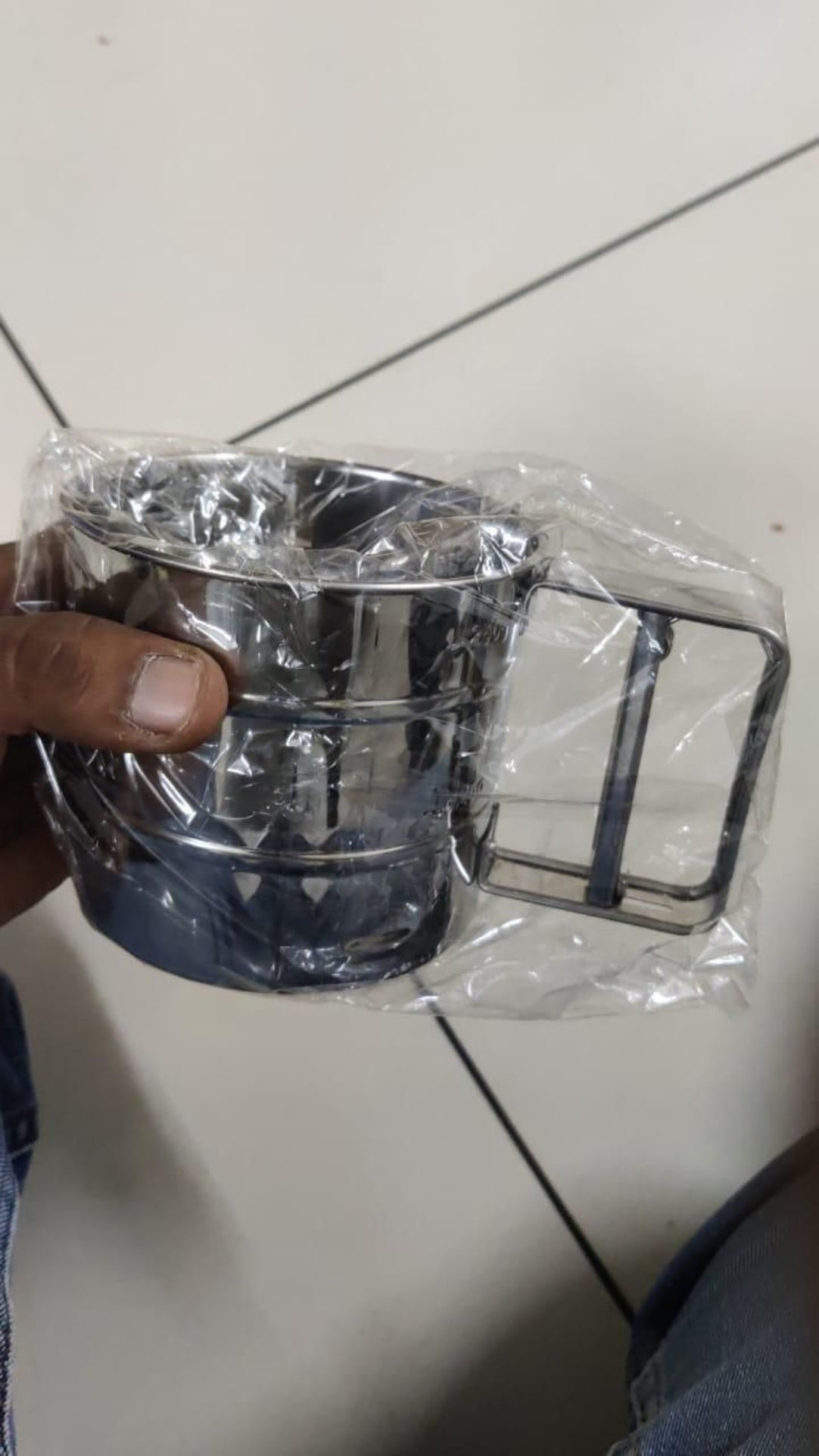 Metallic container with handle held by a hand on a tiled floor