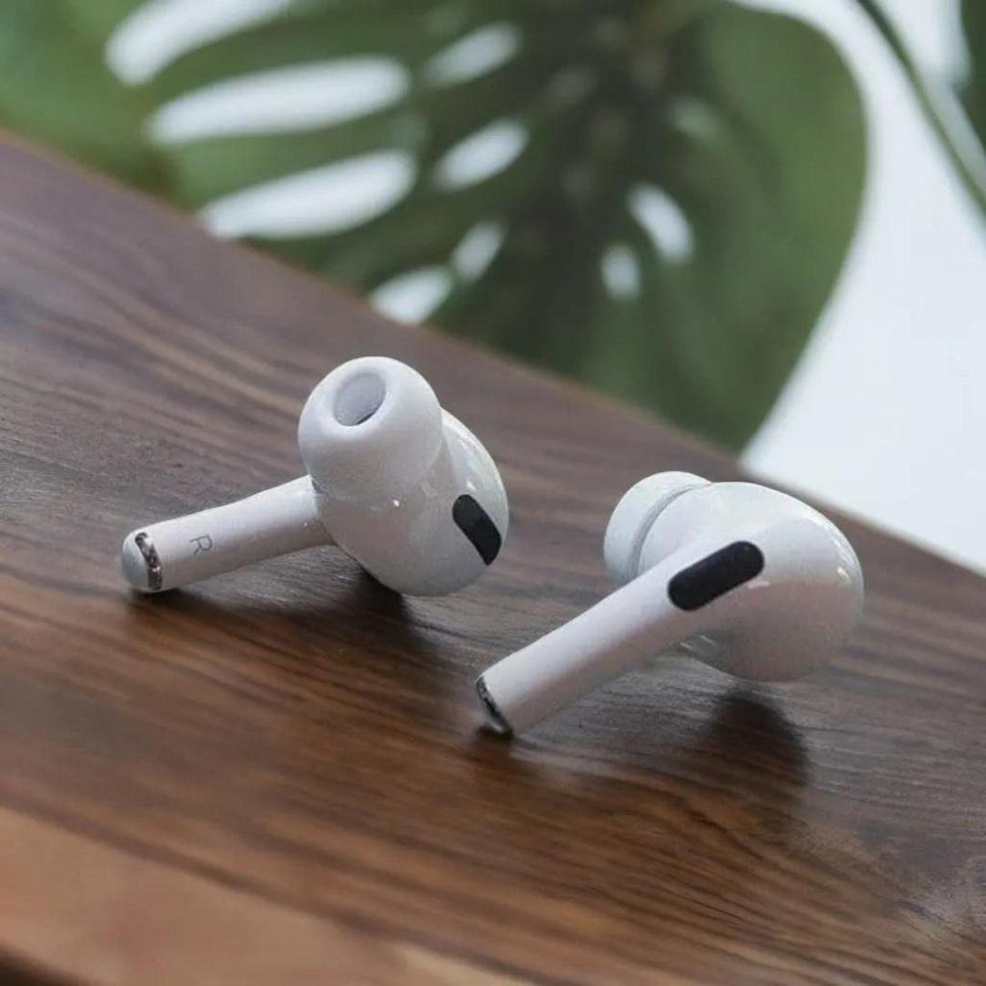 White wireless earbuds on a wooden surface with a blurred green plant in the background