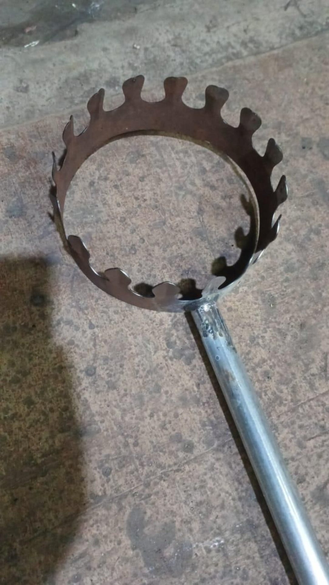 Metal fire pit tool with a circular, toothed design on a concrete surface