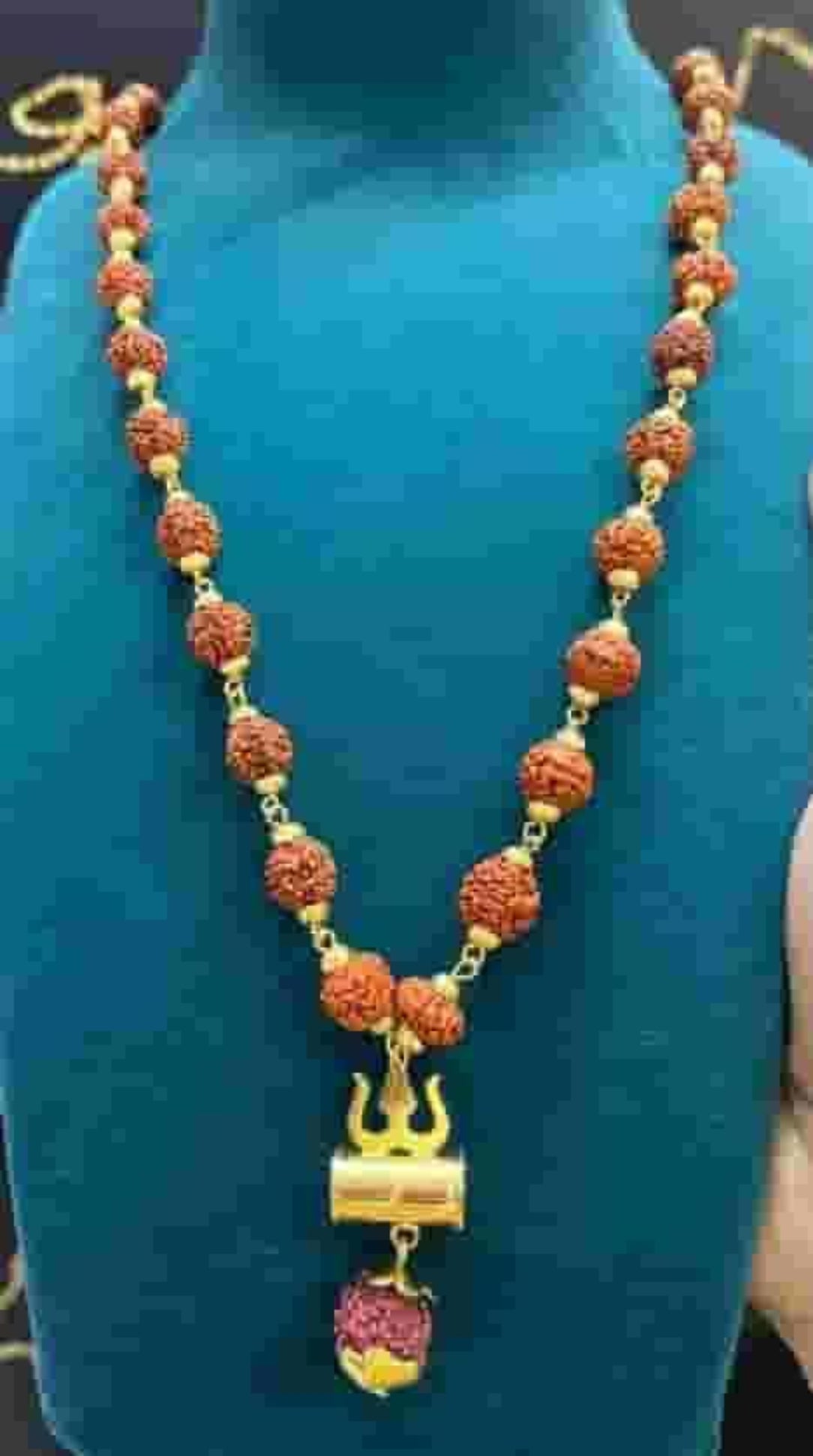 Necklace with orange beads and a gold pendant on a blue mannequin