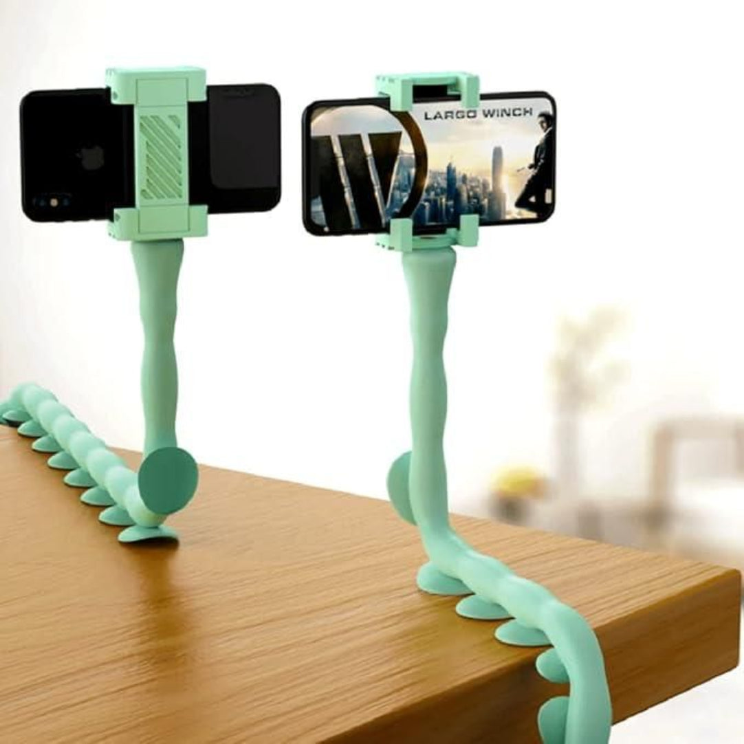 A green octopus-shaped mobile phone stand holding a smartphone in an extended pose on a wooden surface.