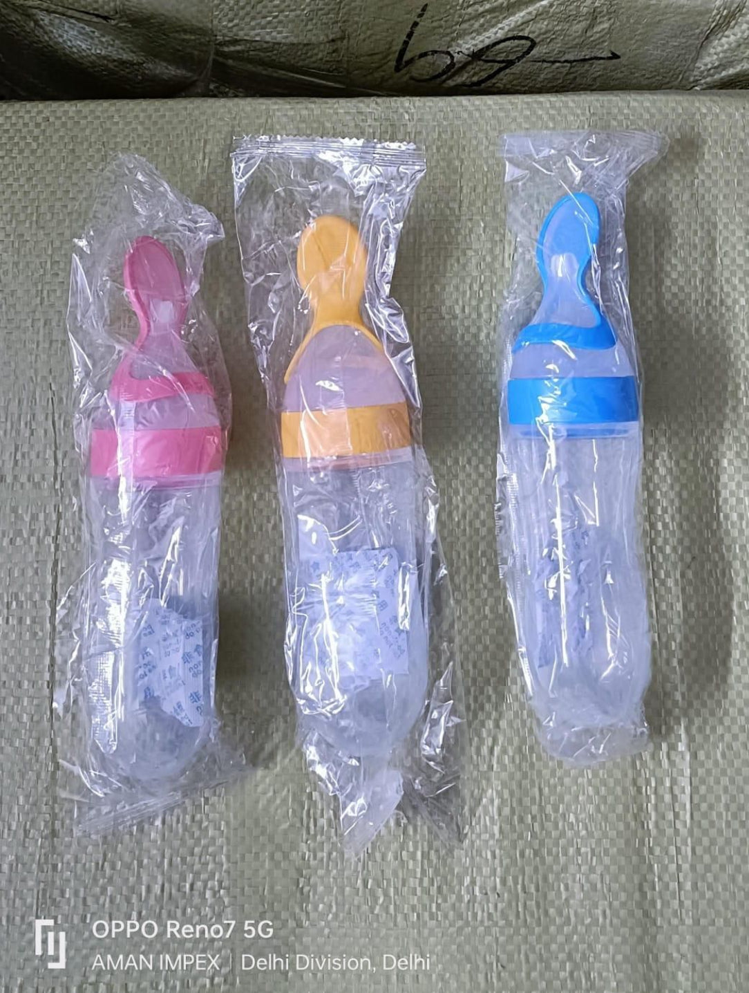 Three baby feeding bottles with colorful nozzles in clear packaging on a textured surface.