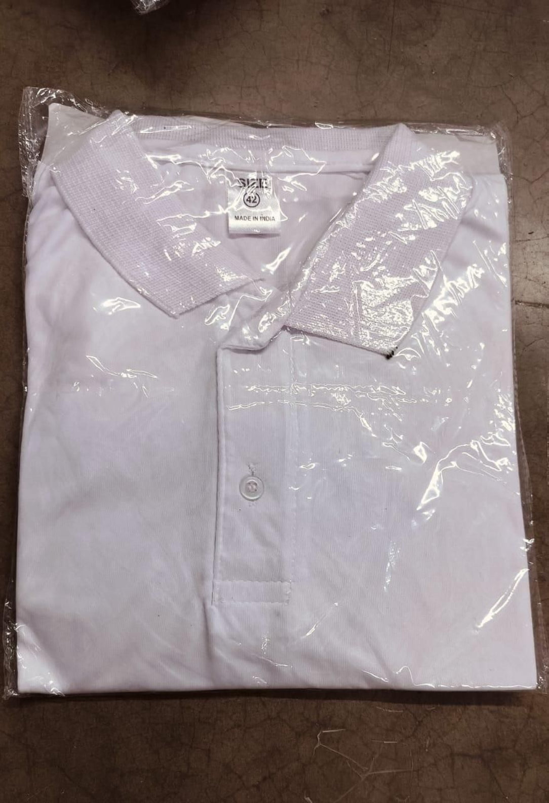 White shirt with a collar and buttons, partially wrapped in clear plastic on a brown surface.