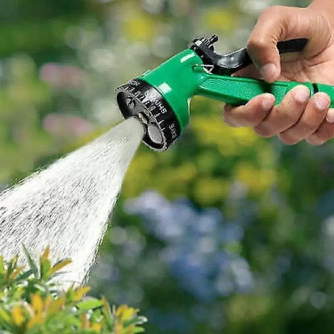 Hand holding a green garden hose nozzle spraying water with a blurred garden background