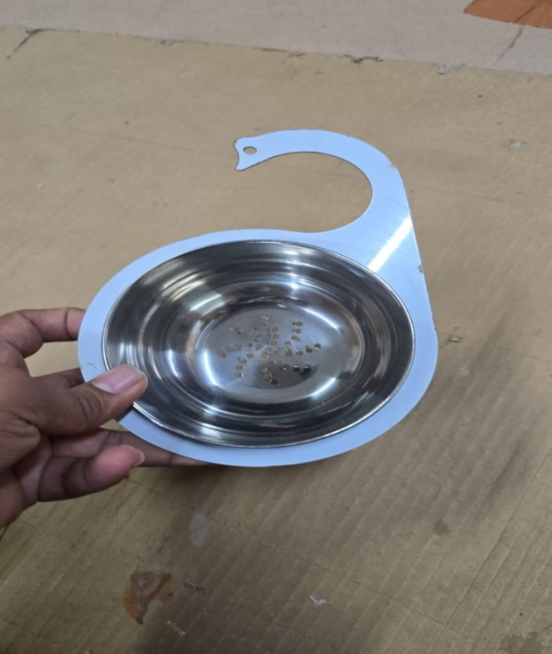 Metallic bowl with a white rim held by a hand on a cardboard background