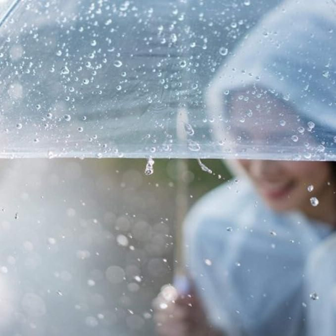 Person holding a transparent umbrella with water droplets against a blurred background