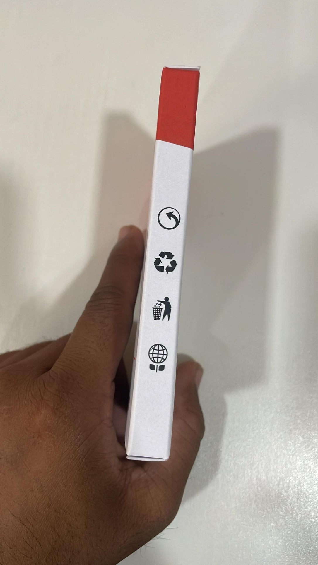 Hand holding a white and red box with recycling symbols on a light gray background