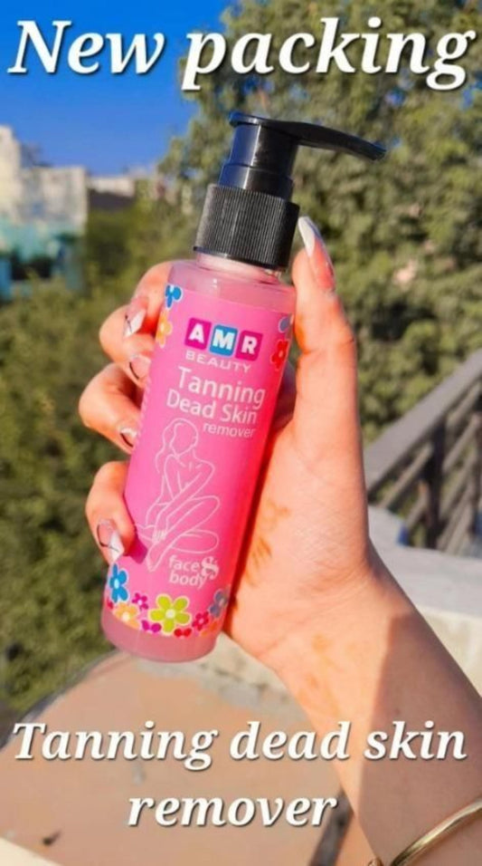 A hand holding a pink bottle of 'Tanning Dead Skin Remover' with a label featuring a woman and text, against a backdrop of a clear blue sky.