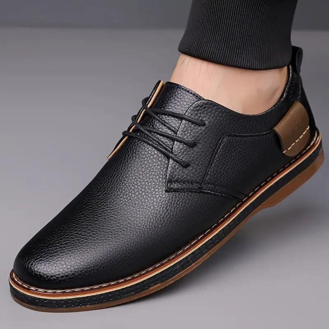 Black leather shoe with brown accents on a gray background