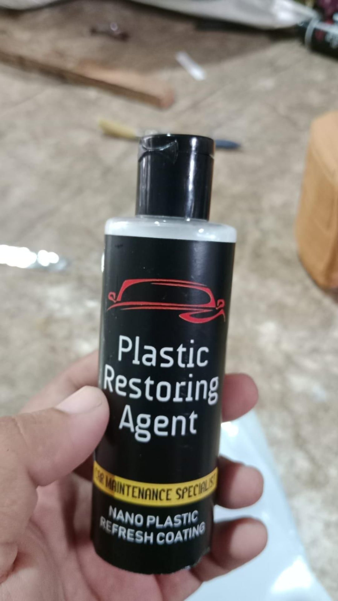 Bottle of plastic restoring agent held by a hand on a blurred background