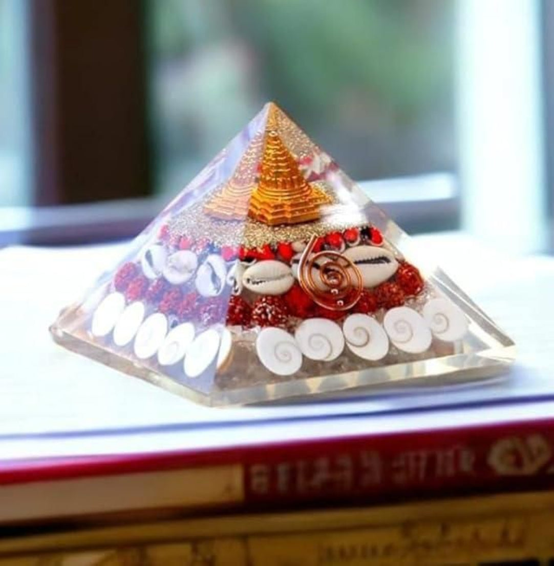 A crystal wealth Gomati Chakra Shree Yantra pyramid with a triangular base and a tapered top, decorated with colored beads and flowers, placed on a book.