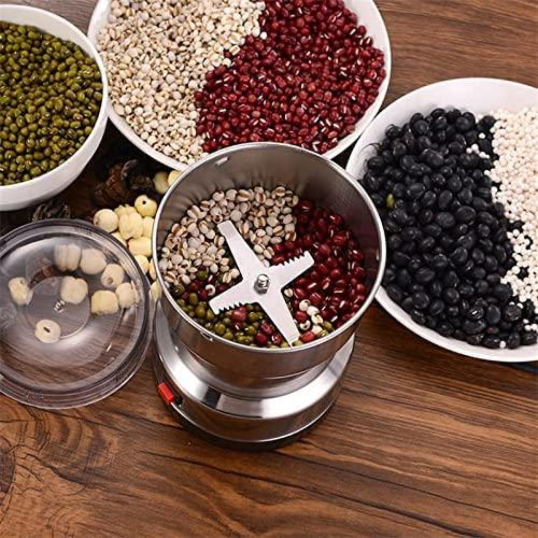 Stainless steel spice grinder with various seeds and grains on a wooden surface