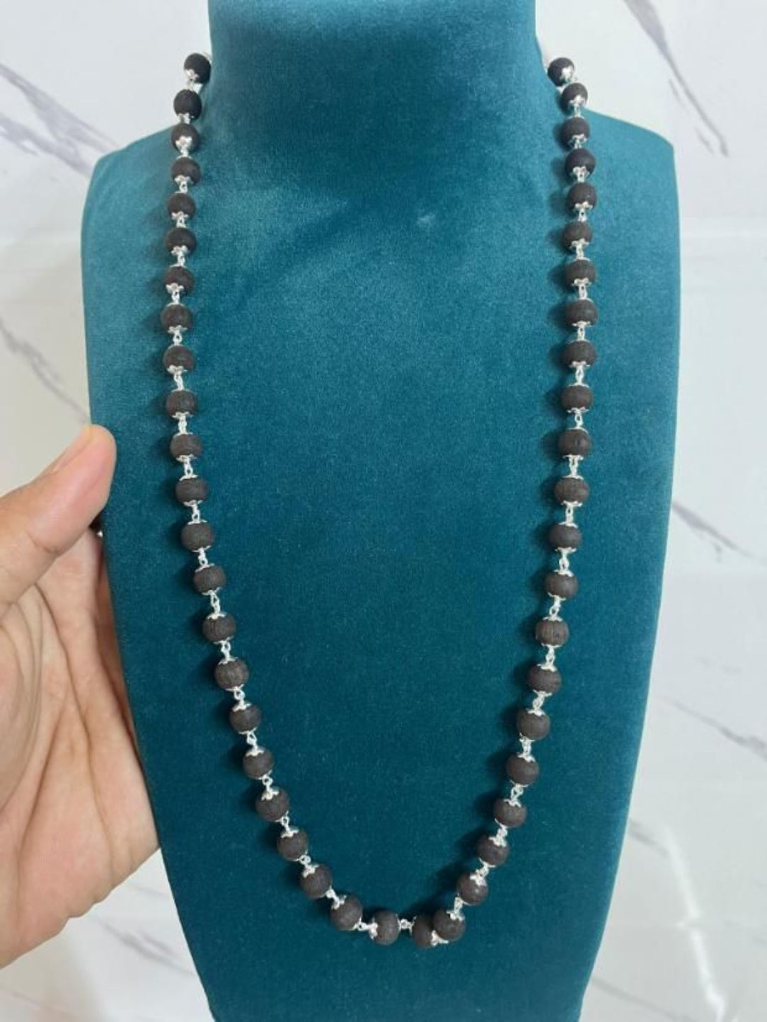 Necklace with brown and silver beads on a blue stand