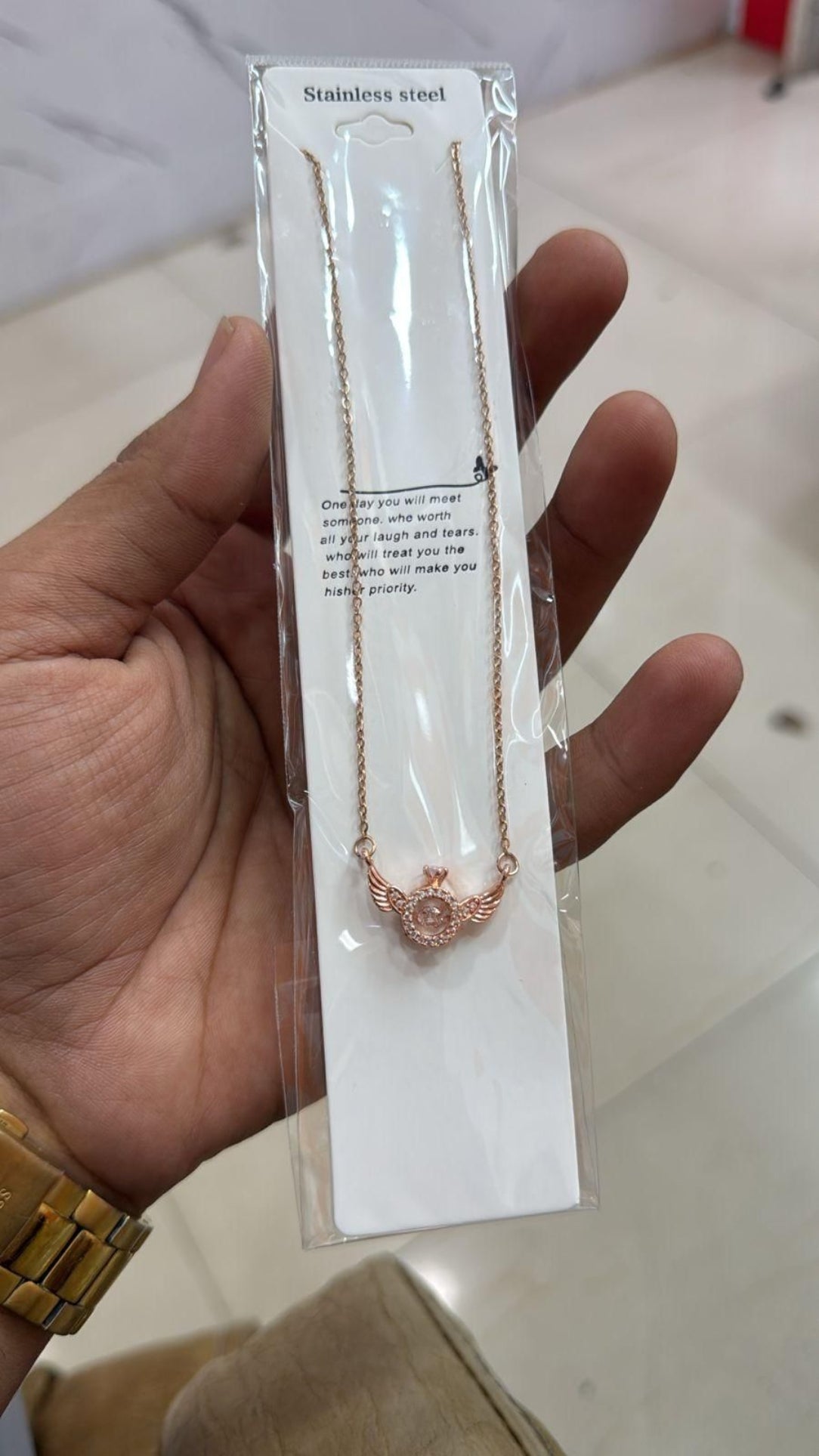 Necklace with rose gold butterfly pendant on a white card held by a hand.