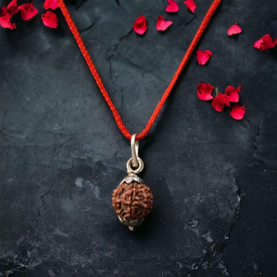 Brown pendant on a red string with red petals on a dark surface