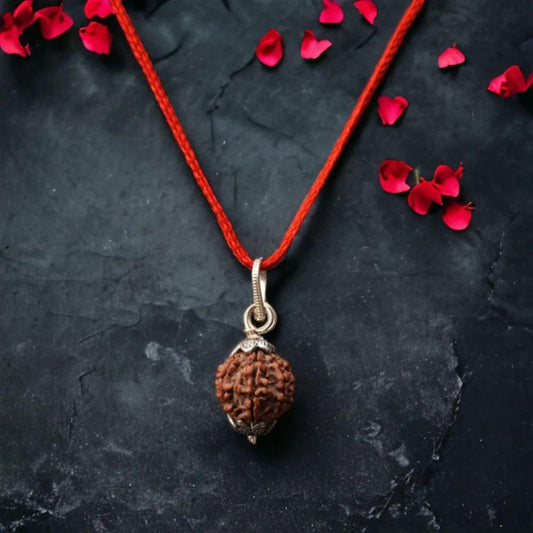 Brown pendant on a red string with red petals on a dark surface