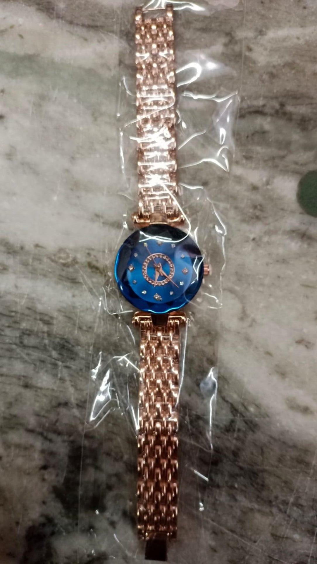 Rose gold watch with blue face in clear plastic packaging on a marble surface