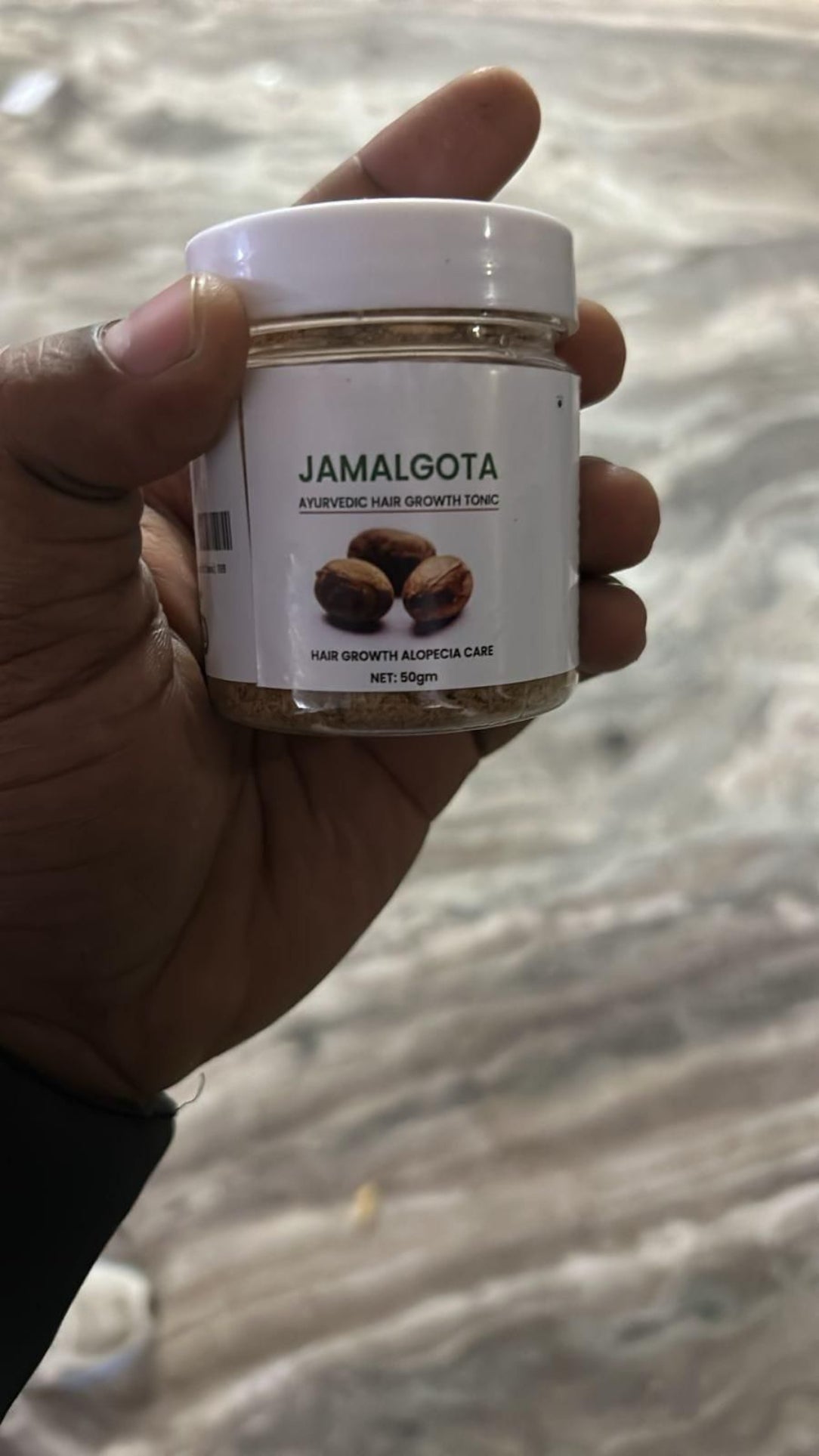 Hand holding a jar labeled 'Jamalgota' against a blurred background