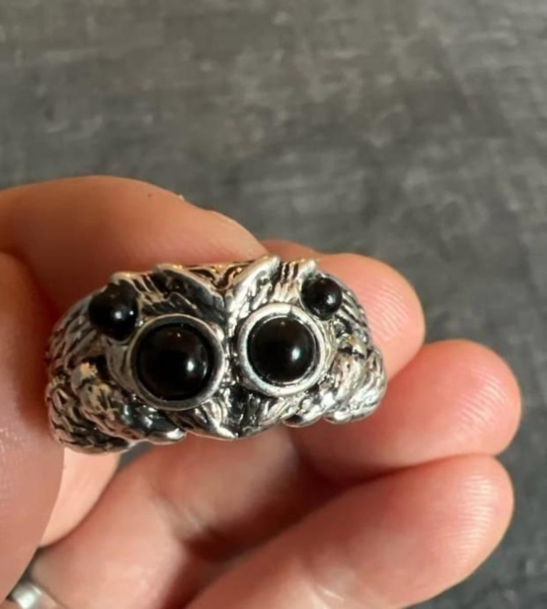 Silver owl ring with black gemstones held in a hand against a gray background