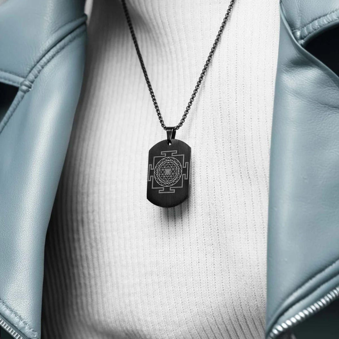 Black pendant necklace with a geometric design on a white shirt with a light blue jacket.
