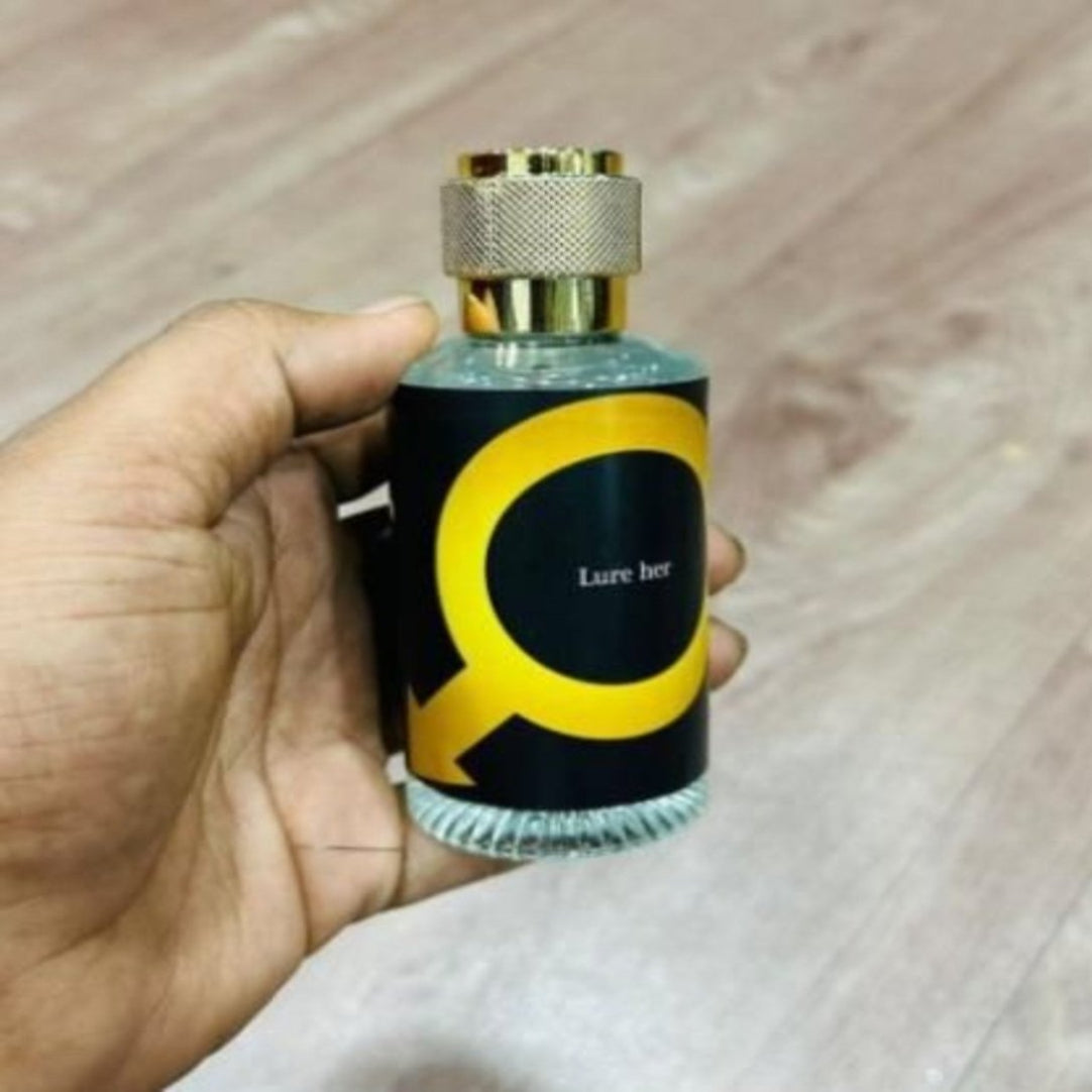 Hand holding a perfume bottle with a black and yellow label on a wooden surface