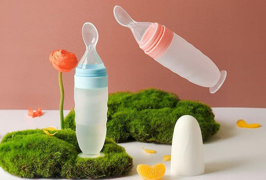 Two baby bottles with spoons on a surface with green grass and flowers.