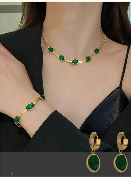 A woman wearing an oval green crystal pendant necklace, matching bracelet, and earrings with gold-colored metal accents.