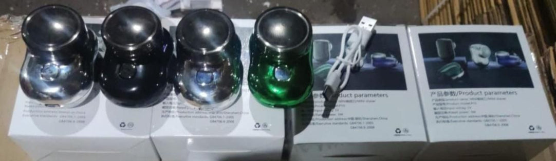 Set of metallic containers with a green one on a white surface, with a box and additional items in the background.