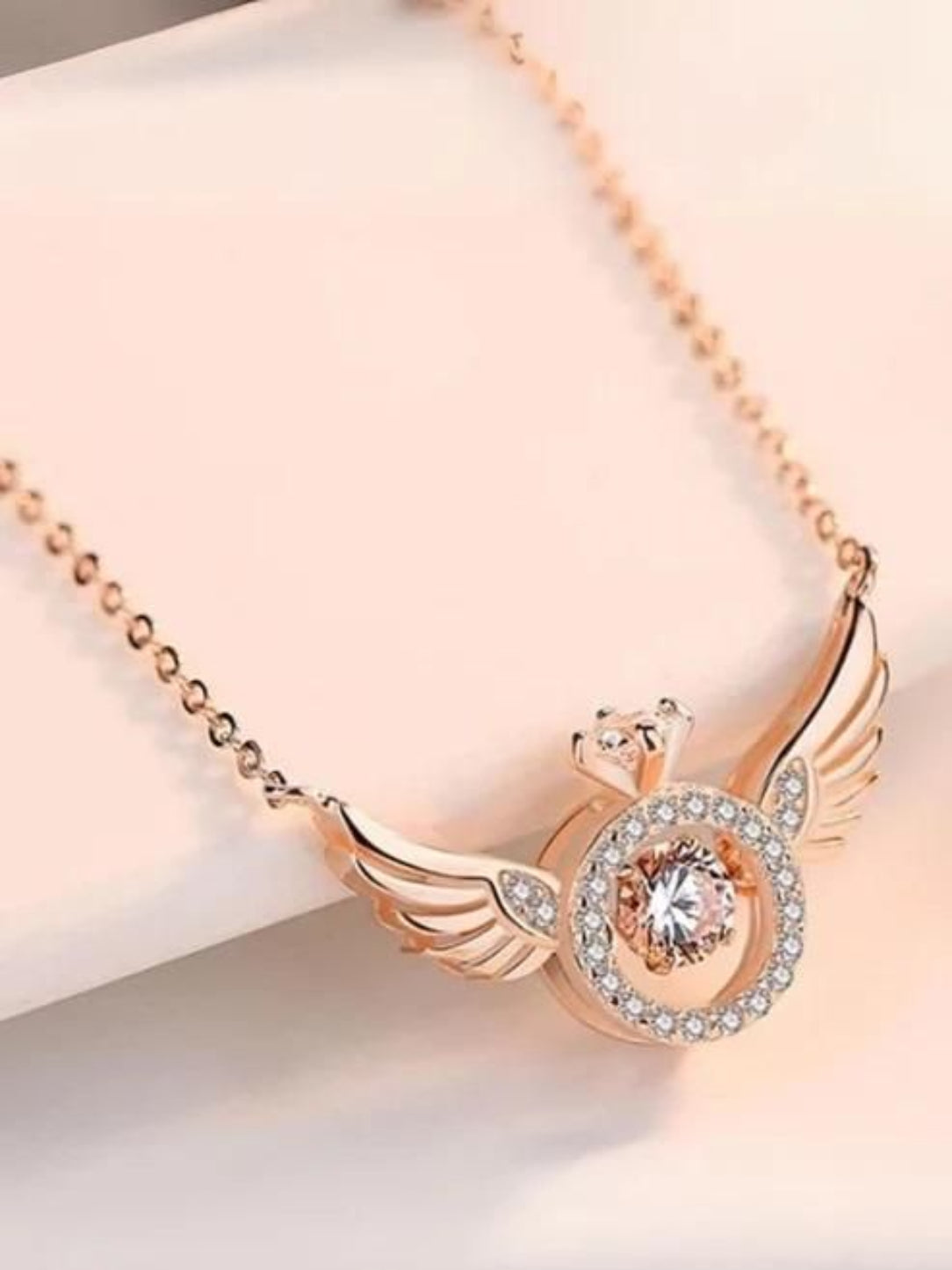 Rose gold necklace with angel wing design on a light background