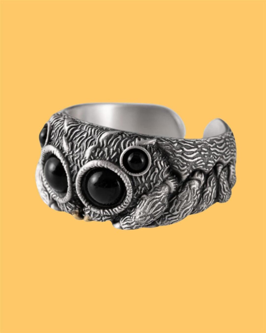 A silver-colored alloy ring with a detailed design resembling a spider's head, featuring black eyes.