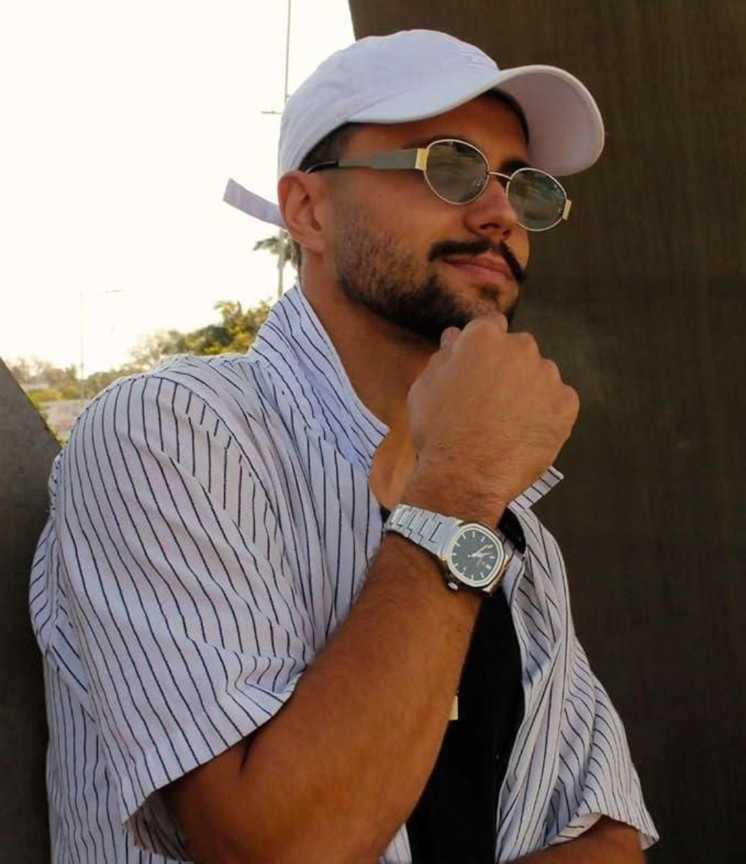 Man wearing a white cap, sunglasses, and a striped shirt with a watch.