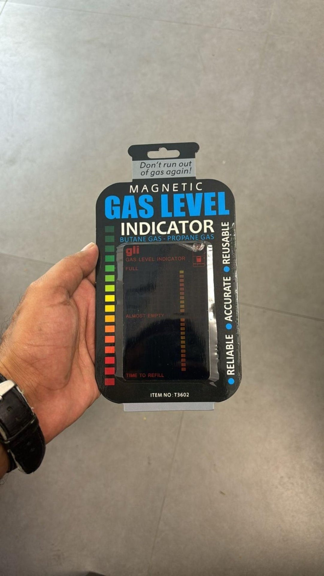 Magnetic gas level indicator in packaging held by a hand against a neutral background