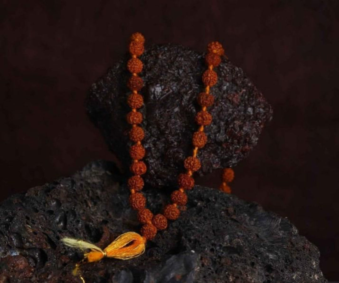 A Rudraksha Jaap Mala with 108 beads placed on a dark textured surface, with a bright yellow string tied at one end.