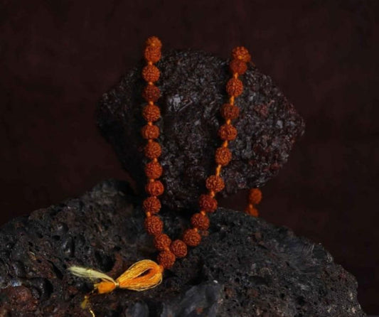 A Rudraksha Jaap Mala with 108 beads placed on a dark textured surface, with a bright yellow string tied at one end.