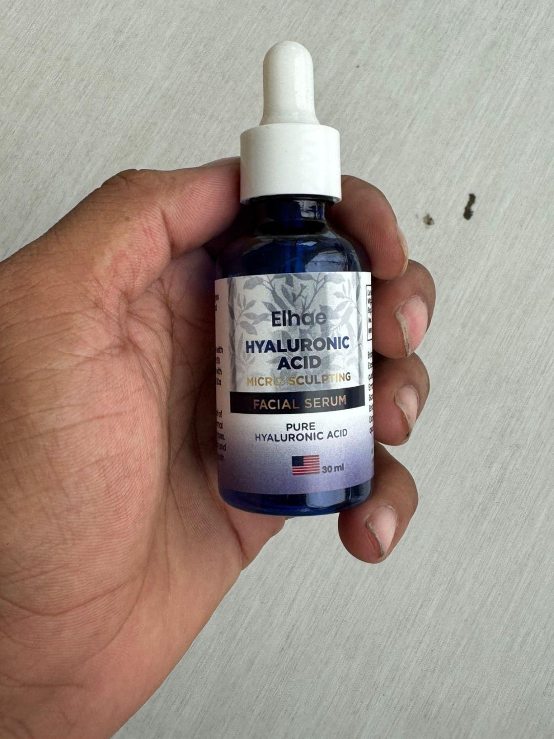 Hand holding a bottle of Eligo Hyaluronic Acid facial serum against a neutral background