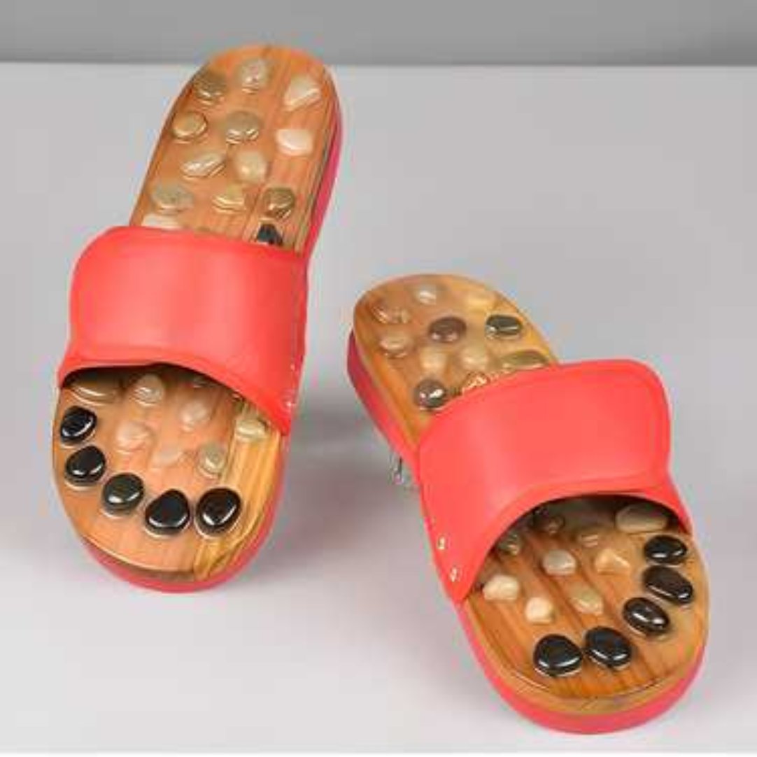 A pair of red acupressure natural stone slippers with a wooden sole and black stones embedded for reflexology.