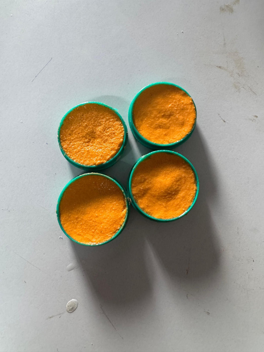 Four containers with orange powder on a light gray surface
