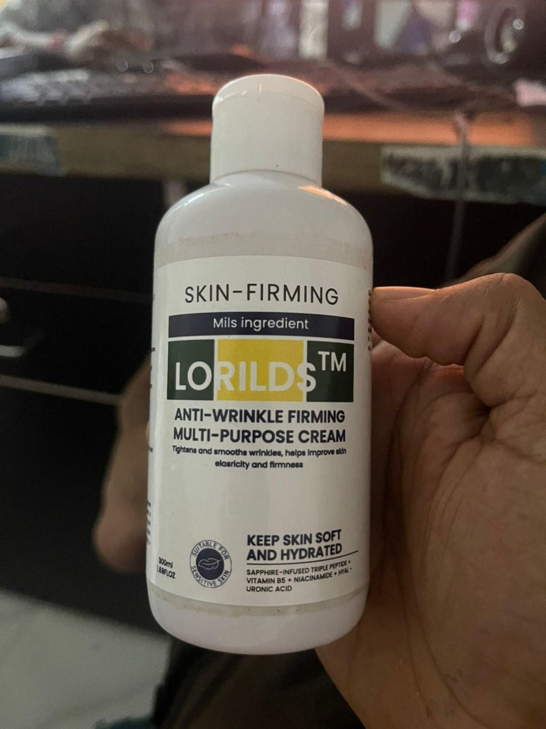 Bottle of Lorilds skin-firming cream held in a hand with a blurred background
