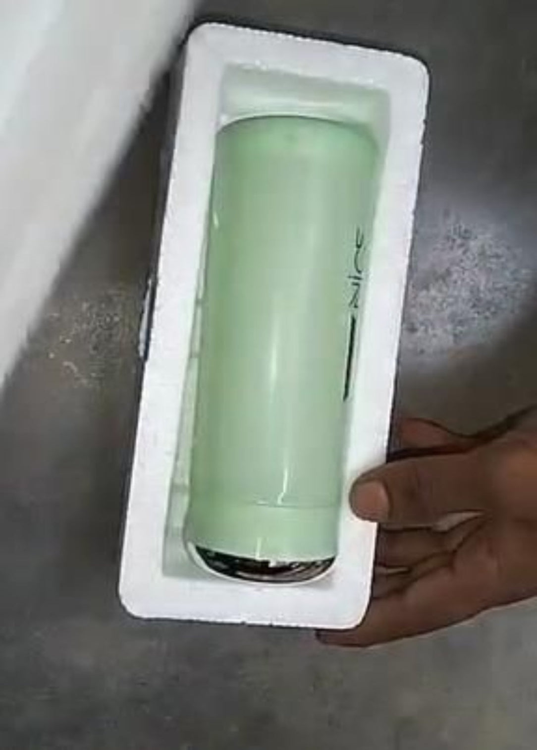 Green cylindrical object in a styrofoam block held by a hand on a concrete floor.