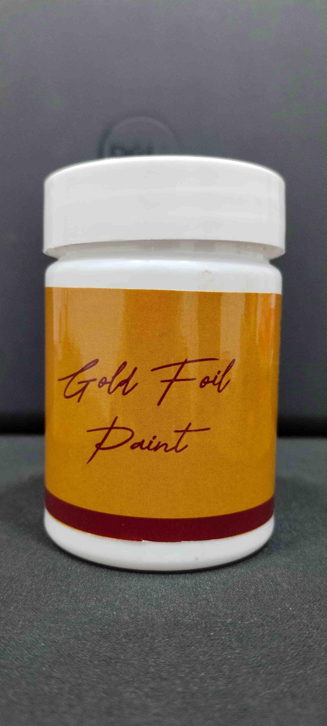 Jar of gold foil paint with a white lid on a gray background