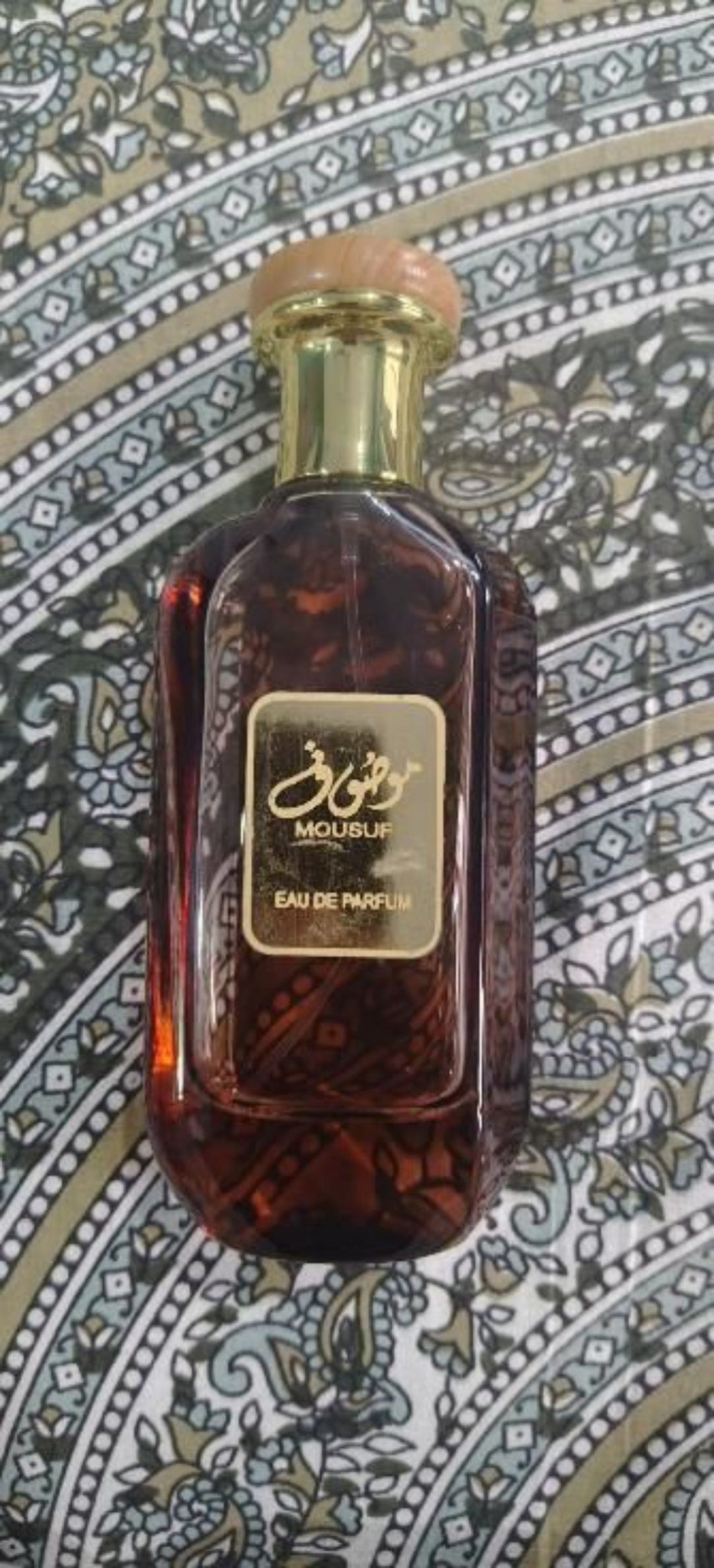 Brown perfume bottle with gold cap on a patterned fabric background
