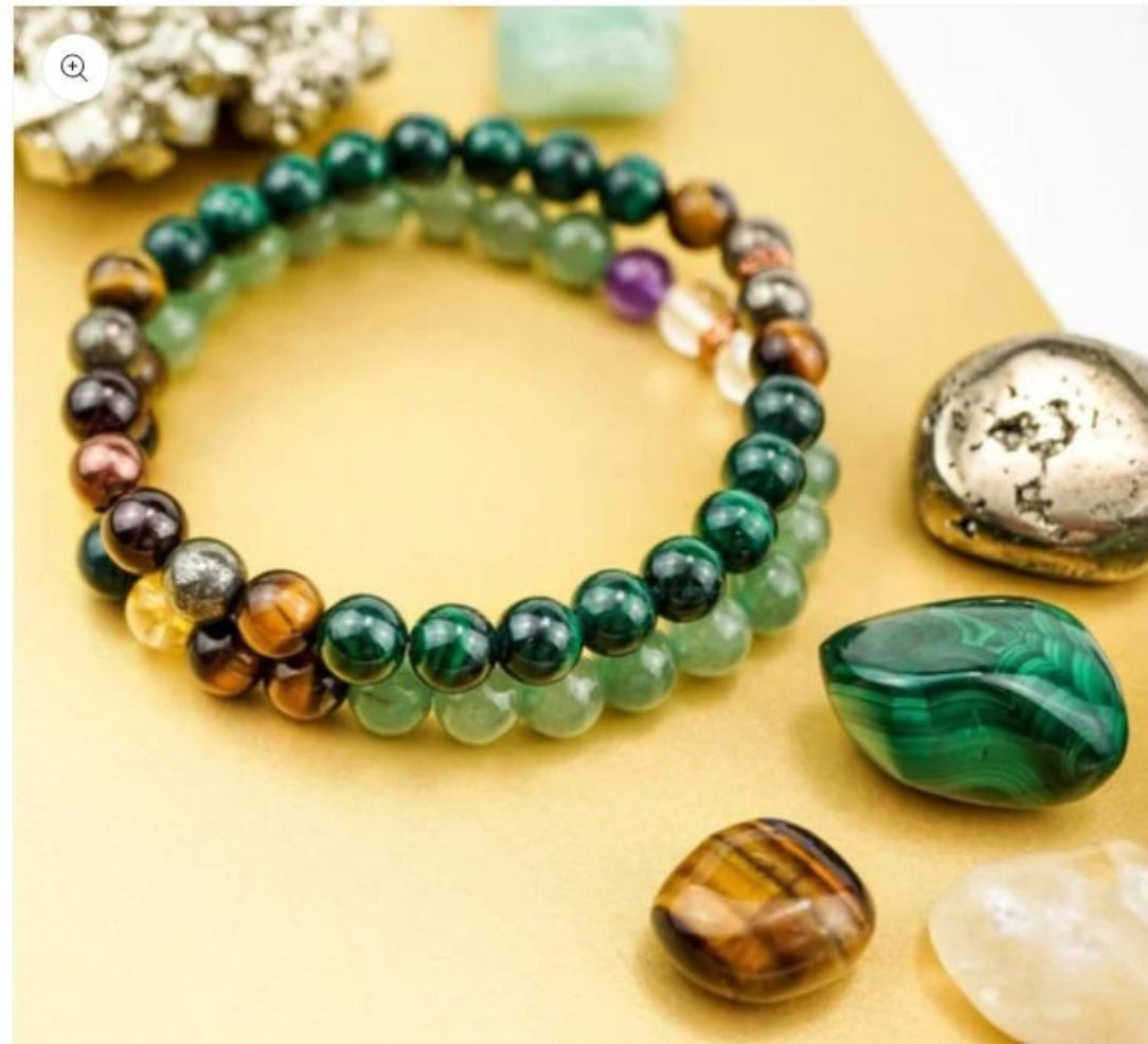 A collection of beaded bracelets in various colors laid out next to some stones and crystals, presumably part of the 'Money Magnet Bracelets' product.