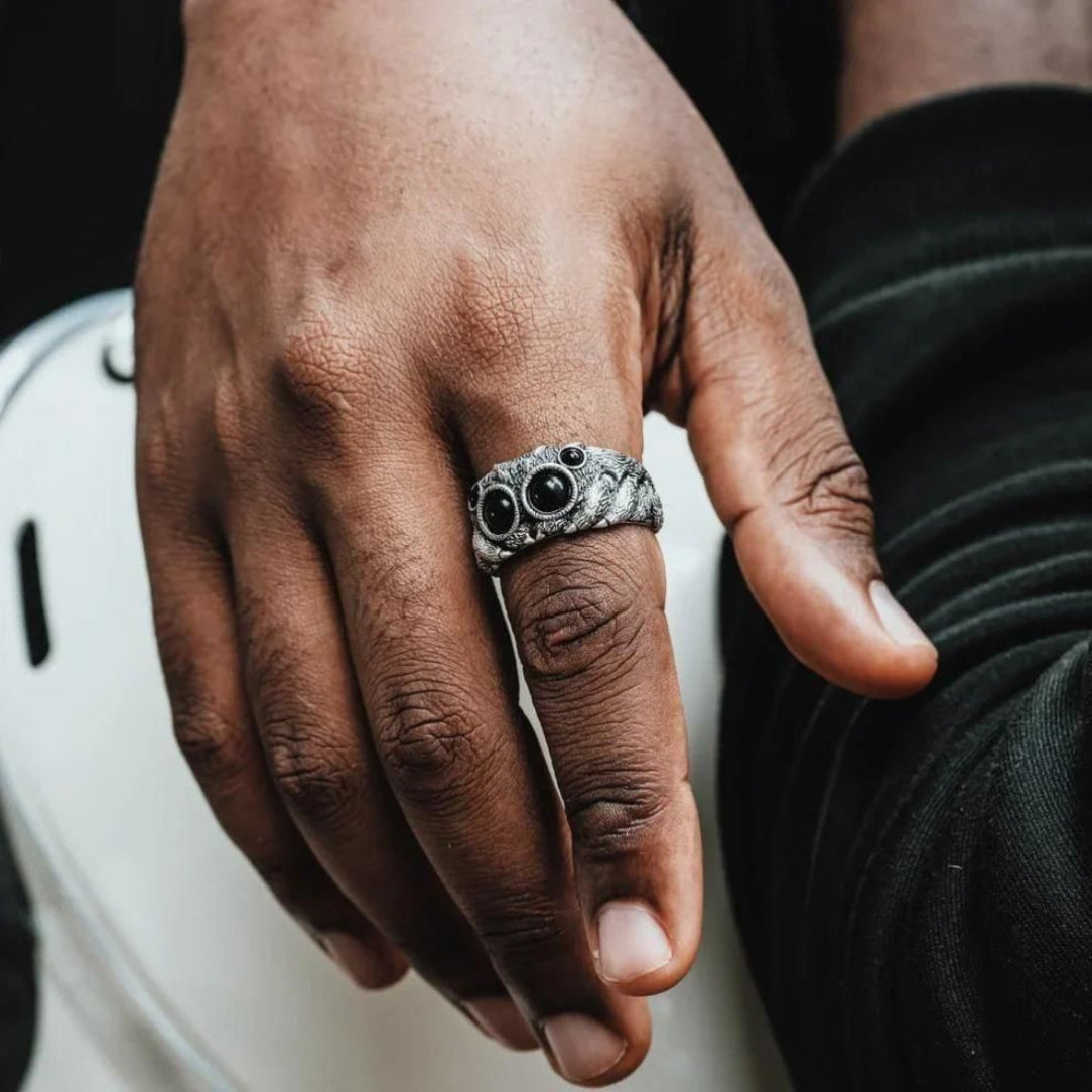 Hand wearing a silver ring with black stones on a blurred background