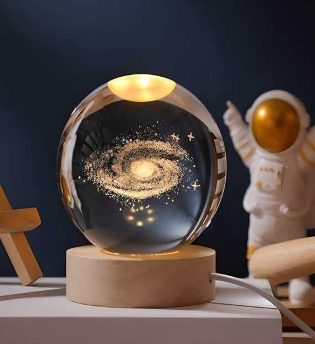 A crystal-clear 3D engraved lamp ball with a warm glow, placed on a wooden stand, with a space-themed design visible inside the ball.