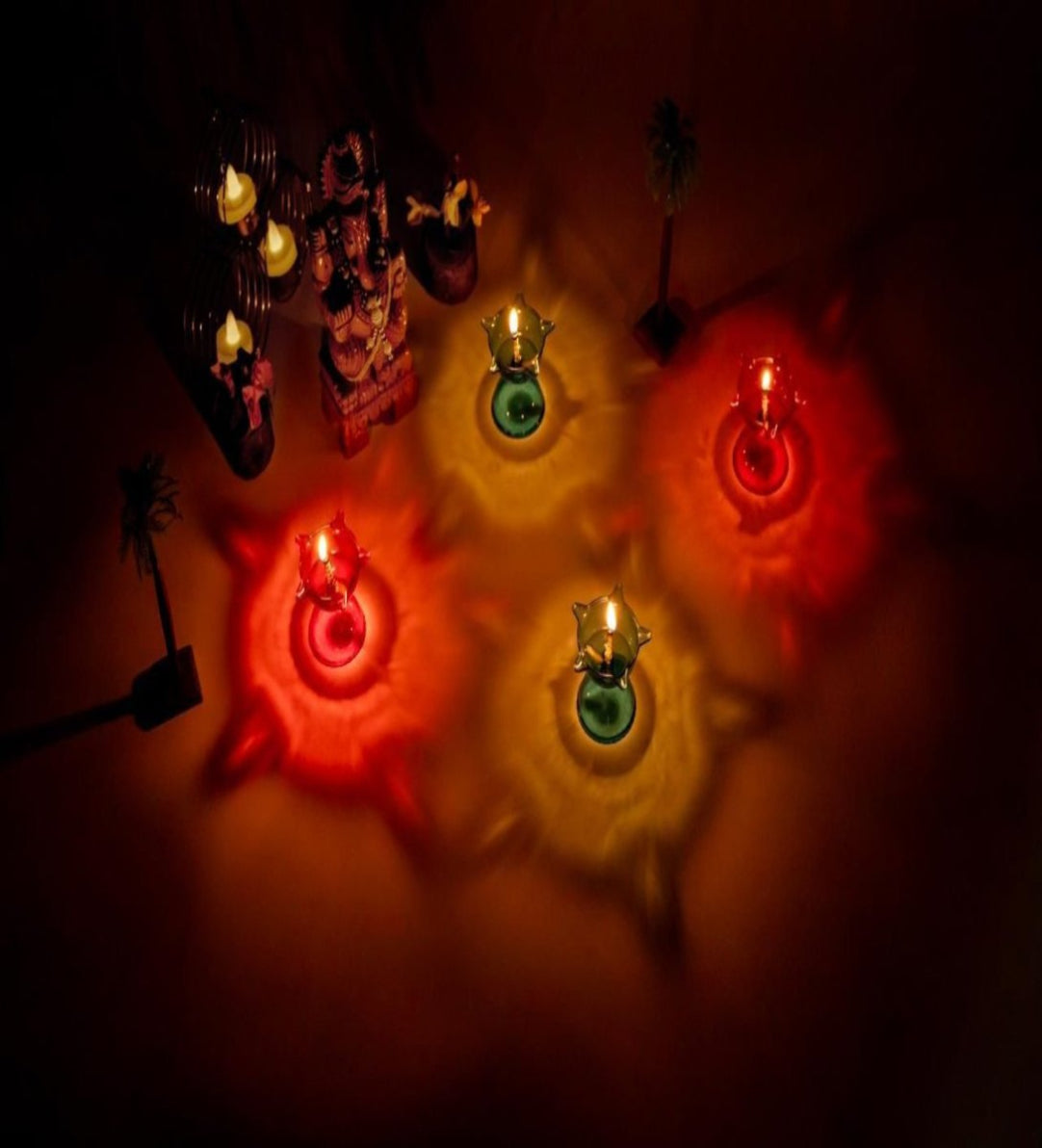 A set of five colorful 3D reflective diyas with lit wicks, placed on a surface with a warm glow.