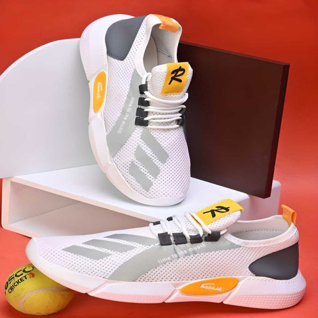 A pair of white casual shoes with yellow accents, displayed with a pair of tennis balls and a red box in the background.