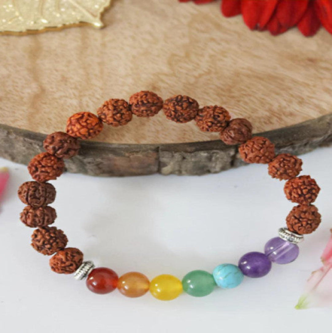 A Rudraksha bracelet with round brown beads and multicolored beads representing the seven chakras, displayed on a wooden surface.