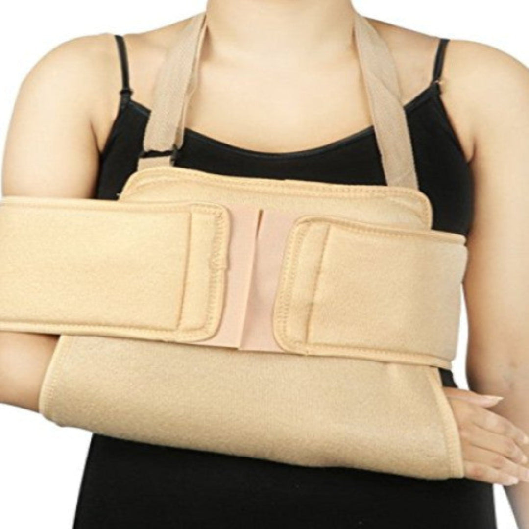 A person wearing a beige U-shaped shoulder immobilizer box pack designed to support the arm and shoulder area.