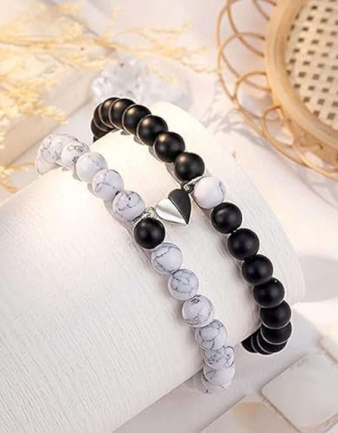Two bracelets, one with black beads and a silver arrow charm, and one with white beads, placed side by side on a white surface.