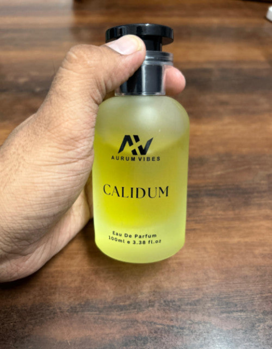 Hand holding a bottle of Aurum Vibes Calidum perfume on a wooden surface
